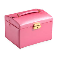 Boîte à bijoux nomade rose poudré avec poignée et fermoir doré, forme rectangulaire arrondie.