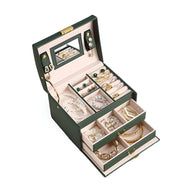 Boîte à bijoux nomade verte, multiples tiroirs ouverts, intérieur beige avec bijoux variés et miroir intégré.