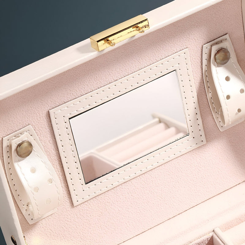 Boîte à bijoux rose poudré en cuir avec miroir intégré et sangles à boutons dorés.