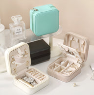 Boîte à bijoux nomade beige avec miroir intégré, compartiments pour bagues et boucles d’oreilles.