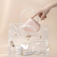 Boîte à bijoux nomade rose avec miroir intégré, petit format, tenue à la main au-dessus d’un sac transparent.
