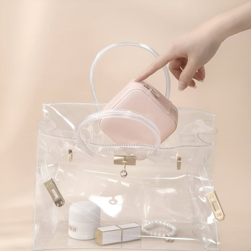 Boîte à bijoux nomade rose avec miroir intégré, petit format, tenue à la main au-dessus d’un sac transparent.