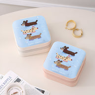 Boîte à bijoux nomade bleue à illustration de chiots joueurs, format carré avec coins arrondis.