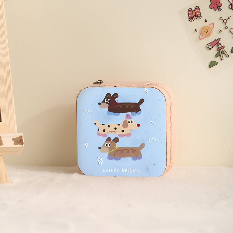 Boîte à bijoux nomade rose avec illustration enfantine de trois chiens joyeux.