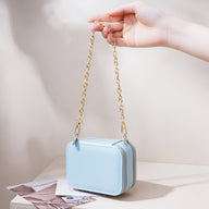 Boîte à bijoux nomade bleue en forme de sac à main avec chaîne dorée élégante.