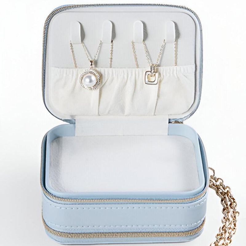 Boîte à bijoux bleue style sac à main avec intérieur blanc et compartiments pour colliers.