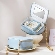 Boîte à bijoux bleue en forme de sac à main avec miroir intérieur et chaîne dorée.