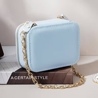 Boîte à bijoux nomade bleue en cuir avec chaîne dorée style sac à main rectangulaire.
