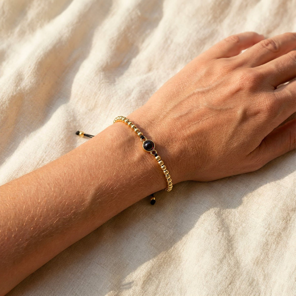 Bracelet à perles métalliques dorées avec perle centrale noire sur cordon noir ajustable porté au poignet.