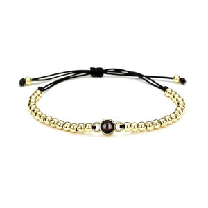 Bracelet à perles métalliques dorées avec perle centrale noire sur cordon noir ajustable.