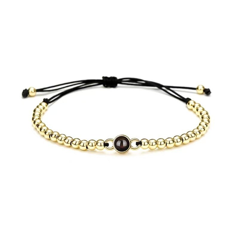 Bracelet à perles métalliques dorées avec perle centrale noire sur cordon noir ajustable.
