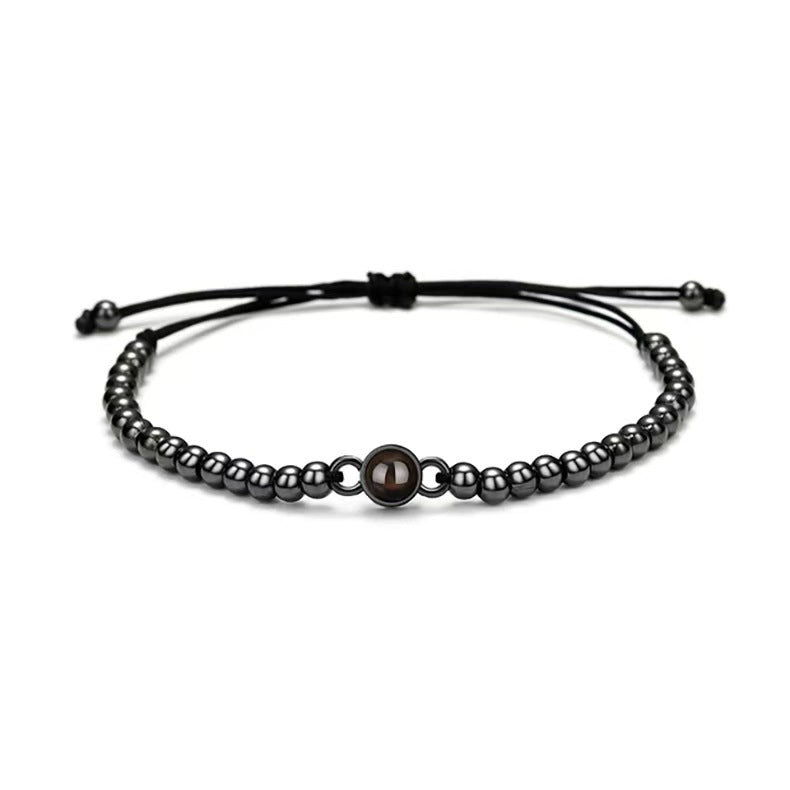 Bracelet réglable en cordon noir avec perles métalliques argentées et perle centrale plus large.