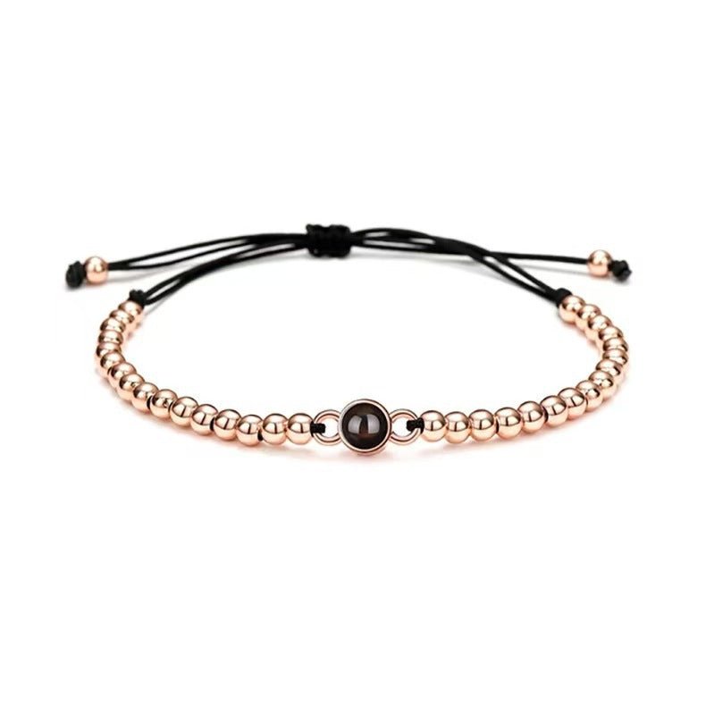 Bracelet réglable à perles métalliques dorées avec projection photo centrale sur cordon noir fin.