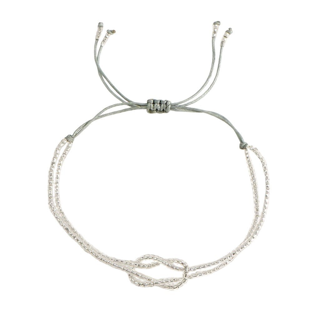 Bracelet fin à perles miyuki blanches avec nœud central en forme de symbole, cordon gris ajustable à coulisse.