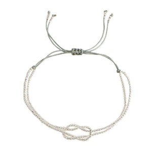 Bracelet fin à perles miyuki blanches avec nœud central en forme de symbole, cordon gris ajustable à coulisse.