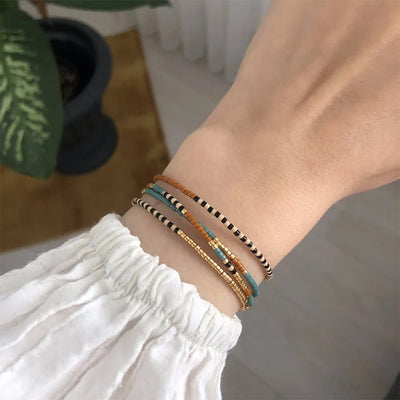 Bracelet à perles Miyuki turquoise, or et brun, cordon ajustable, style bohème chic, porté au poignet.