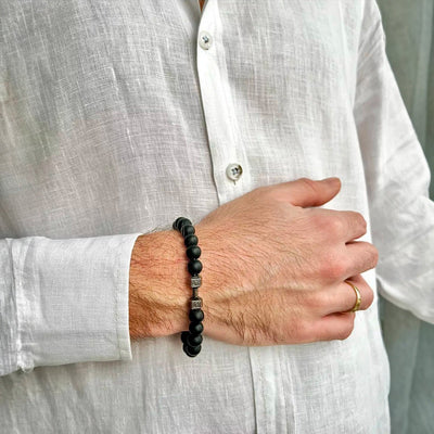 Bracelet homme perles noires mat avec haltère argentée, style musculation, porté au poignet.