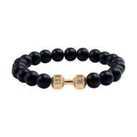 Bracelet perles noires mates avec haltère dorée centrale en acier, style musculation.