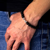 Bracelet à perles noires avec petit pendentif haltère argenté, style musculation, porté au poignet.