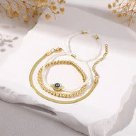 Trio de bracelets en acier inoxydable doré et cordon blanc tressé, perles dorées et breloque œil bleu noir.