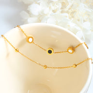 Bracelet ajustable doré en titane avec trois motifs ronds colorés noirs et blancs, chaîne fine délicate.