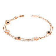 Bracelet ajustable or rosé en titane avec sept motifs colorés ronds alternant noir et blanc, chaîne fine et fermoir.
