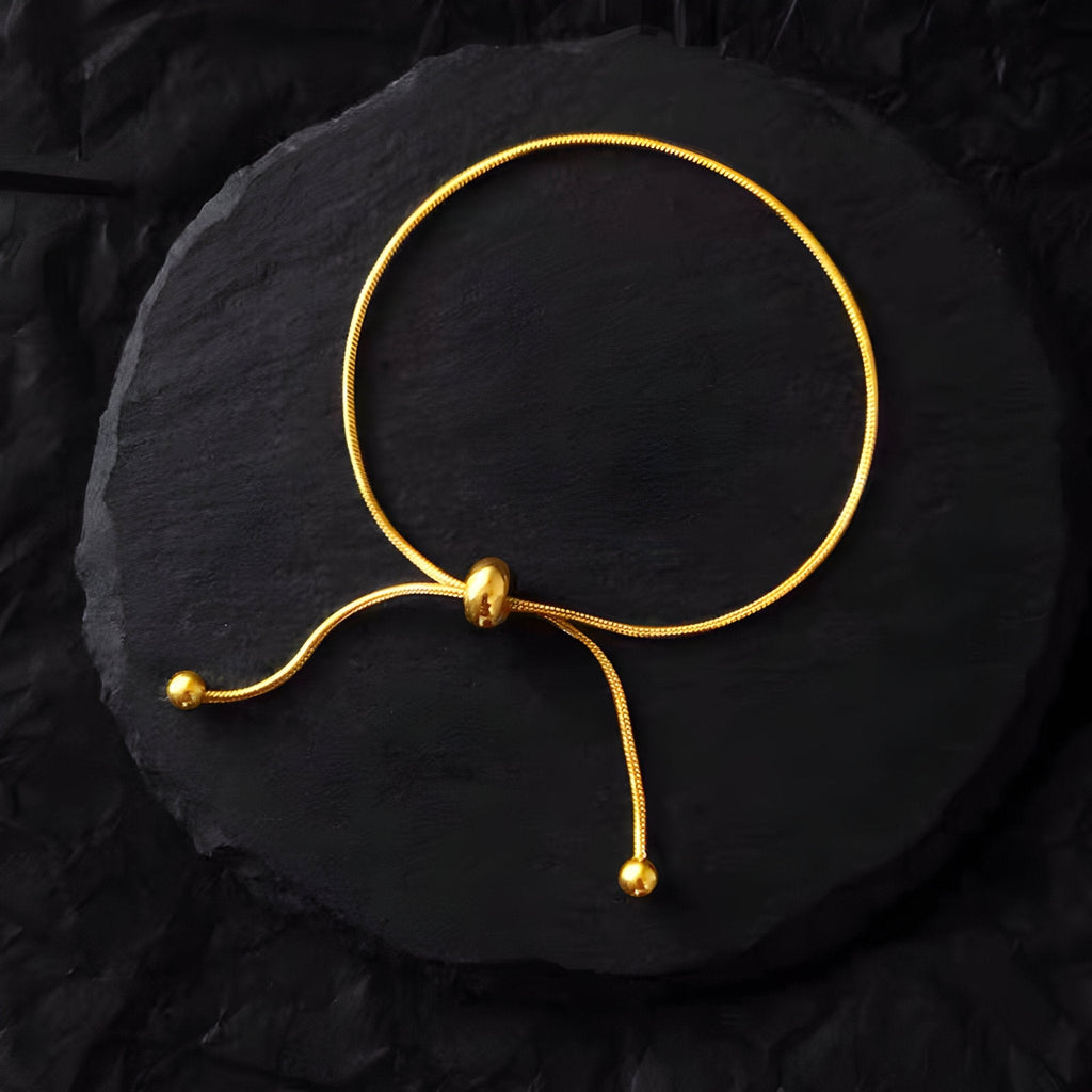 Bracelet ajustable en titane doré avec perles aux extrémités, design minimaliste et élégant.