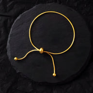 Bracelet ajustable en titane doré avec perles aux extrémités, design minimaliste et élégant.