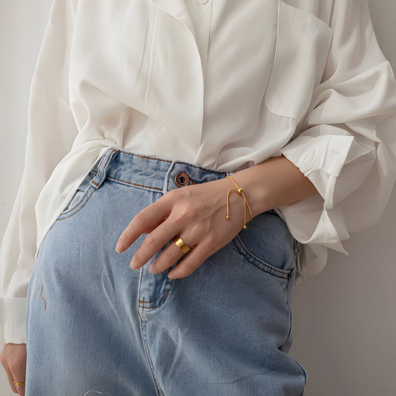 Bracelet ajustable fin en titane doré porté avec bague assortie sur une main féminine, style minimaliste.