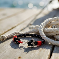 Bracelet ancre noir et rouge en coton avec fermoir en acier inoxydable sur planche en bois.