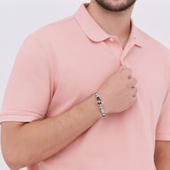 Bracelet ancre en cuir blanc et bleu avec fermoir en acier inoxydable porté au poignet d'un homme en polo rose pâle.