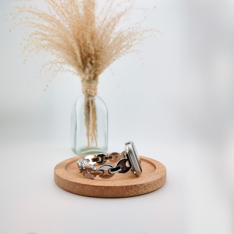 Bracelet Apple Watch en mailles marine argentées, design moderne, posé sur un support en bois rond.