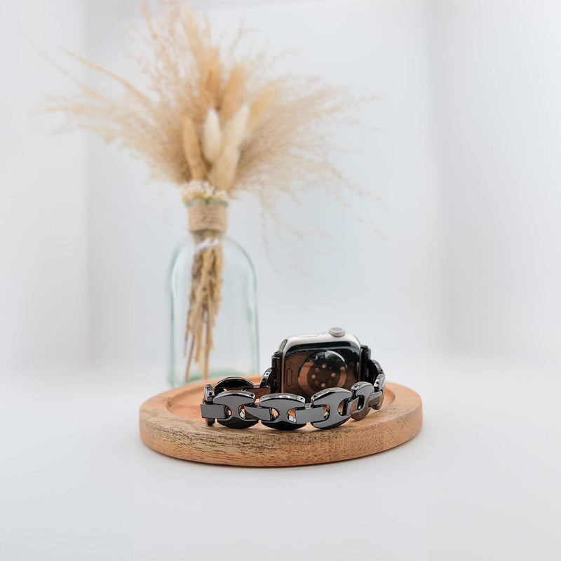 Bracelet maillons marine en acier noir brillant pour Apple Watch, design élégant et moderne, modèle Vily, posé sur un socle.