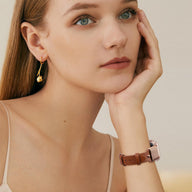 Bracelet Apple Watch en cuir marron avec boucle élégante effet ressort stylisé, porté au poignet féminin.