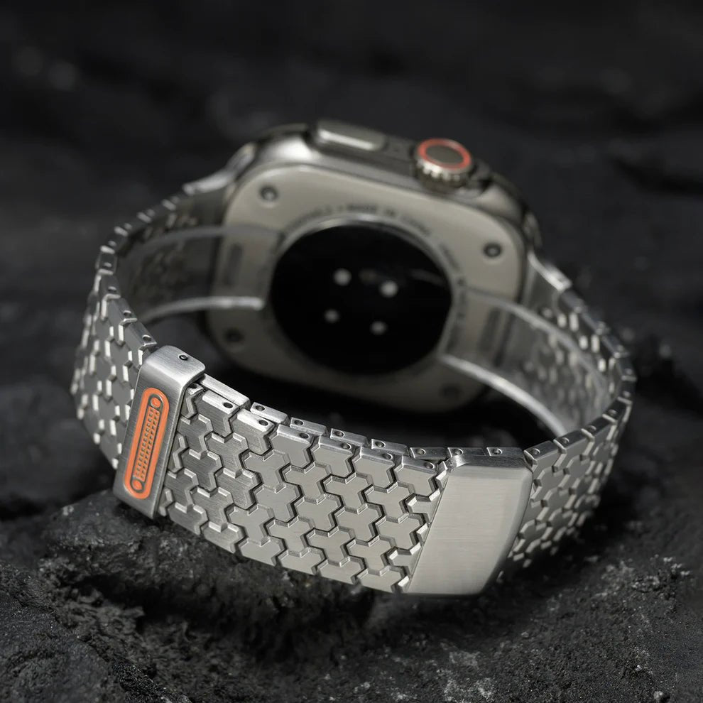 Bracelet Apple Watch en acier inoxydable gris avec maillons hexagonaux et fermeture magnétique noire et orange.