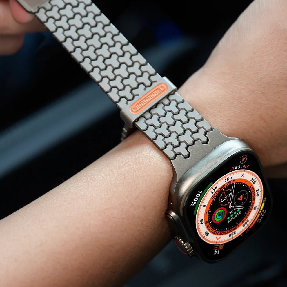 Bracelet Apple Watch en acier inoxydable gris avec maillons hexagonaux noir mat et fermeture magnétique rouge vif.