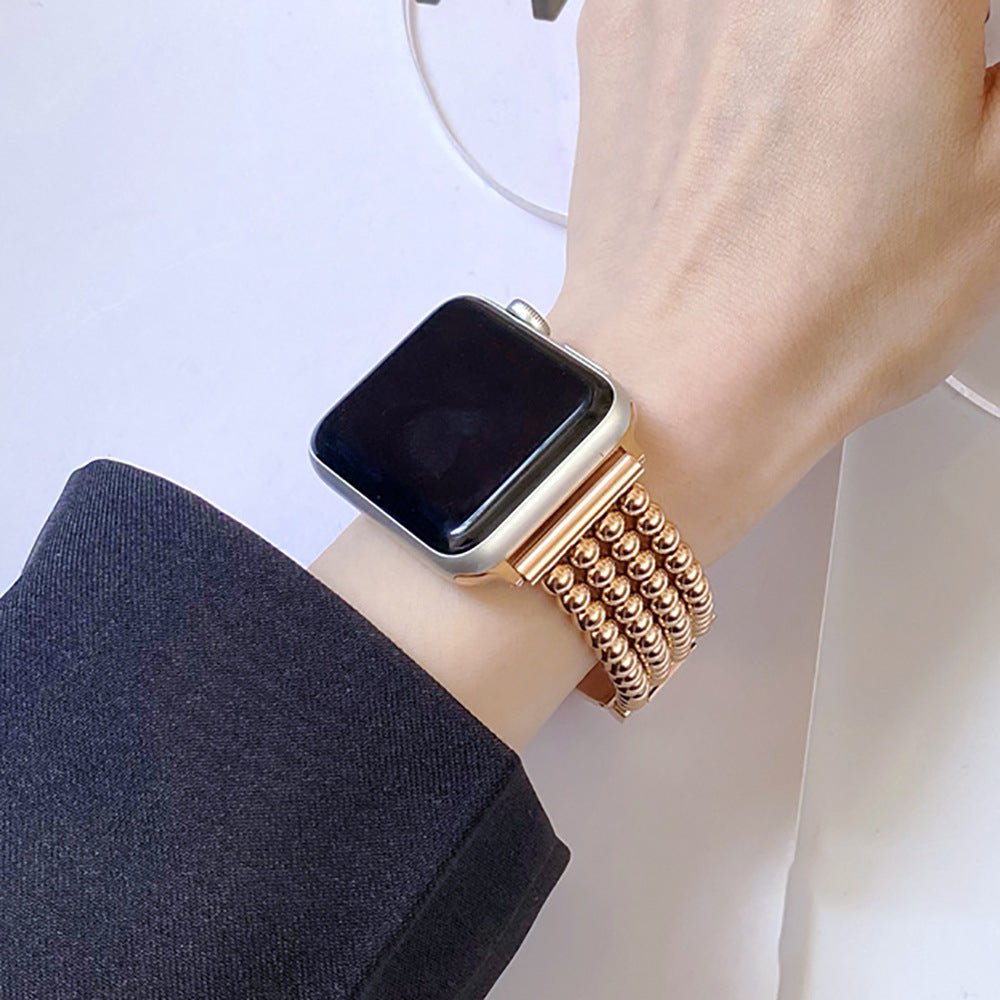 Bracelet Apple Watch en acier inoxydable doré rose avec perles métalliques et fermoir cliquet sécurisé.