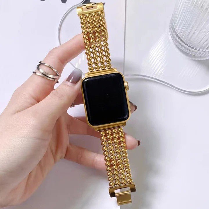 Bracelet Apple Watch en acier inoxydable doré avec finition perles métalliques et fermoir cliquet sécurisé.