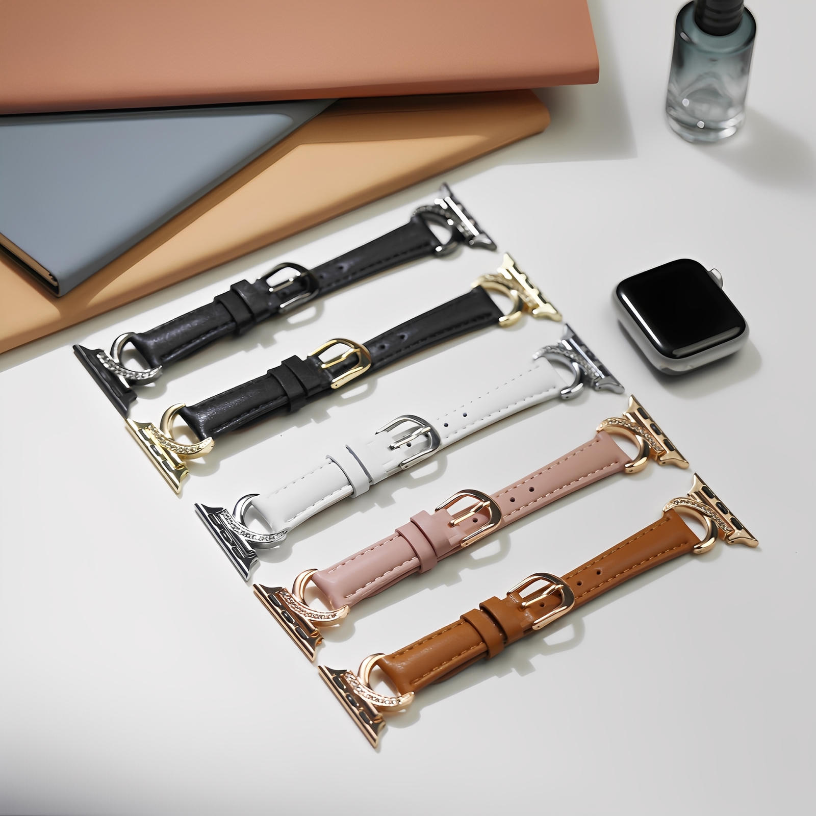 Lot de cinq bracelets Apple Watch en cuir, boucles en C ornées de strass, couleurs noir, blanc, rose, marron et blanc cassé.