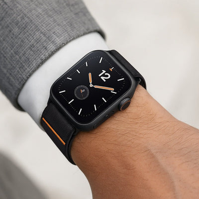 Bracelet Apple Watch en nylon noir avec détail orange, fermeture magnétique invisible, design ergonomique ajusté au poignet.