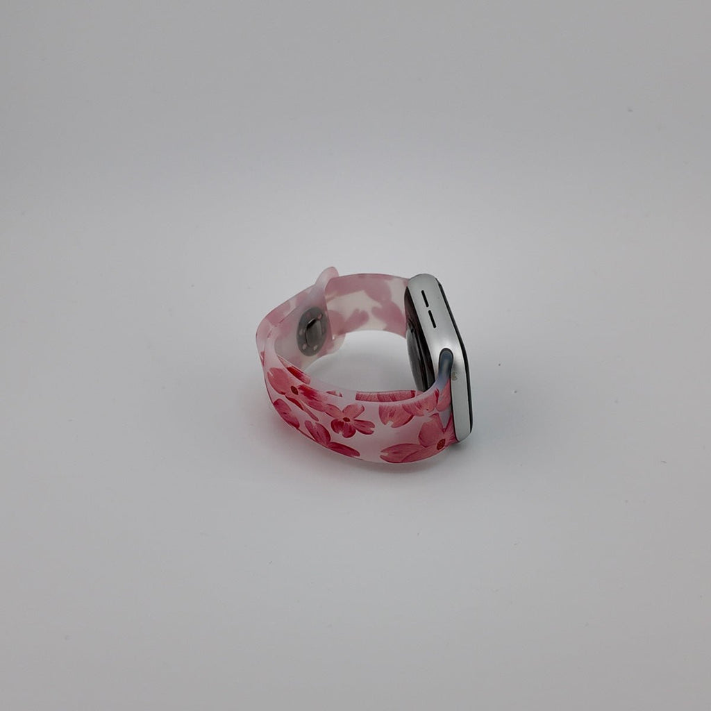 Bracelet Apple Watch en silicone rose clair avec motifs floraux rouges, boucle métallique argentée.