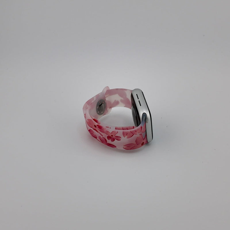 Bracelet Apple Watch en silicone rose clair avec motifs floraux rouges, boucle métallique argentée.