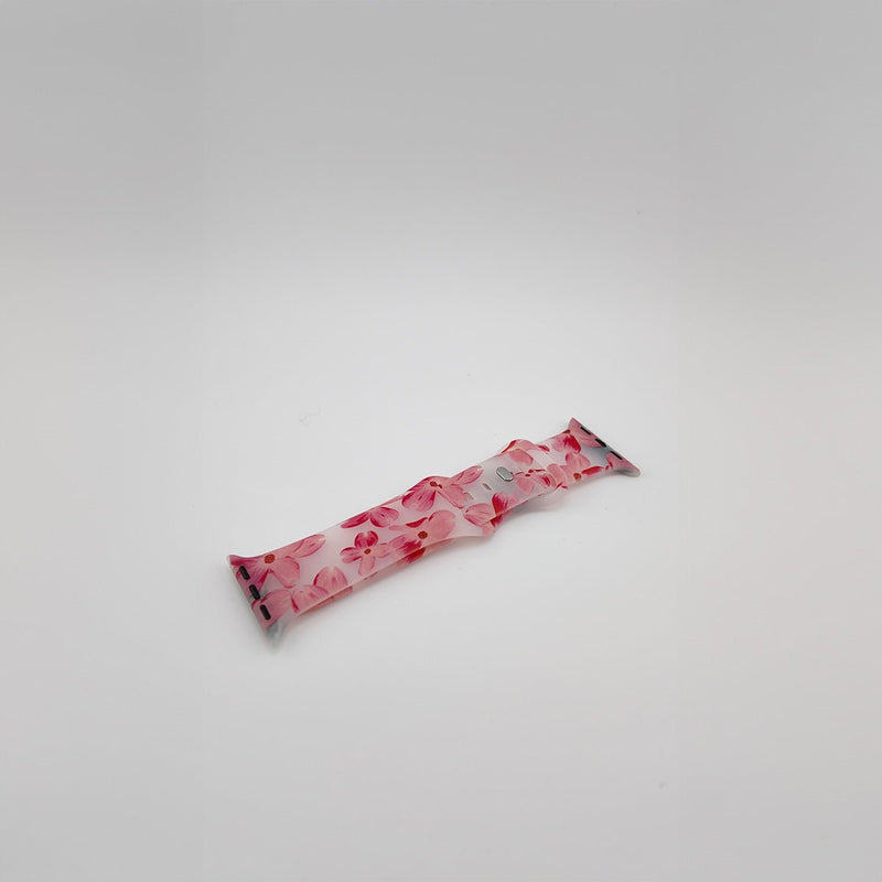 Bracelet Apple Watch en silicone rose clair avec motifs floraux rouges et fermoir métallique noir.