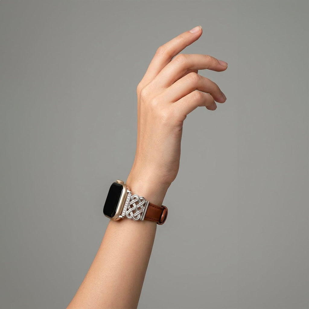 Bracelet montre Apple Watch en cuir marron avec pièce métal argenté tressée et motif noeud celtique décoré de zircons blancs.