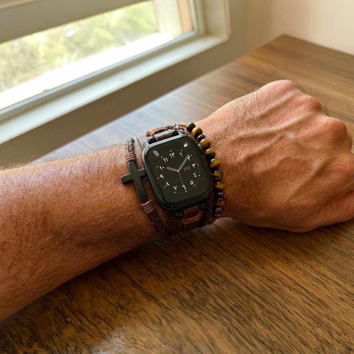 Bracelet multi-rangs simili cuir vegan marron avec perles œil de tigre et croix noire porté avec Apple Watch noire sur.