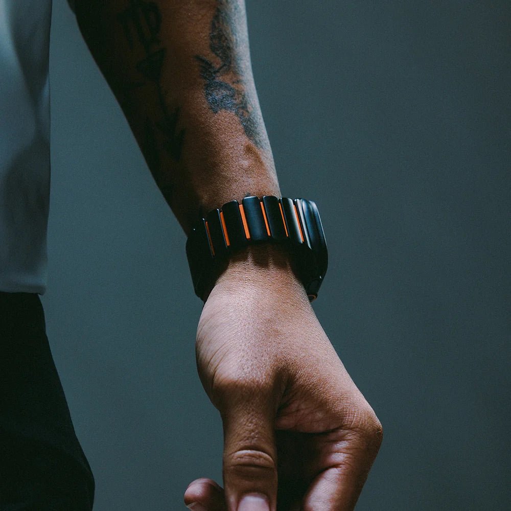 Bracelet Apple Watch Ultra en titane gris foncé avec segments orange, design souple et moderne, porté au poignet.