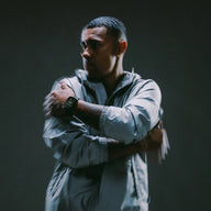 Bracelet Apple Watch Premium titane gris foncé avec lien souple noir porté au poignet gauche sur homme en veste beige.