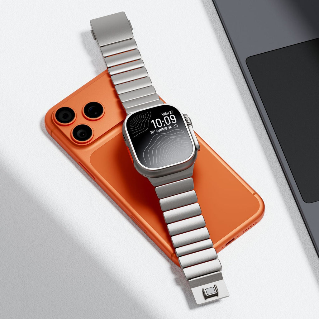 Bracelet Apple Watch en titane Grade 4 argenté, design rigide à maillons, fermoir carré intégré, posé sur un smartphone.