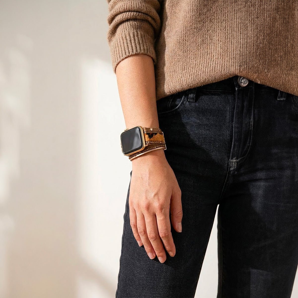 Bracelet Apple Watch simili vegan peau de vache beige et noir avec perles naturelles et fermoir doré, porté au poignet.