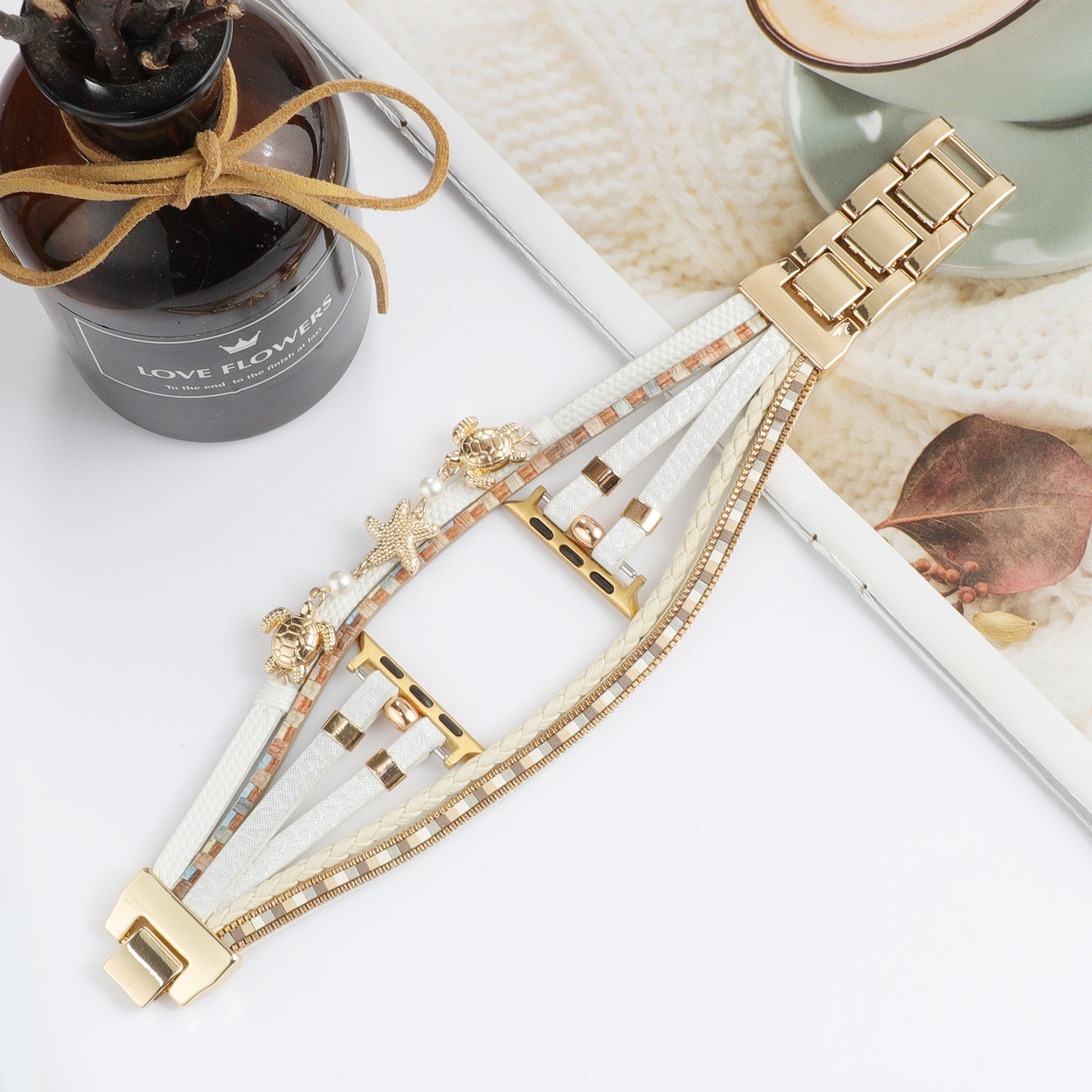 Bracelet Apple Watch doré avec trois liens fins, décoré de perles blanches et breloques tortue et étoile de mer en simili.